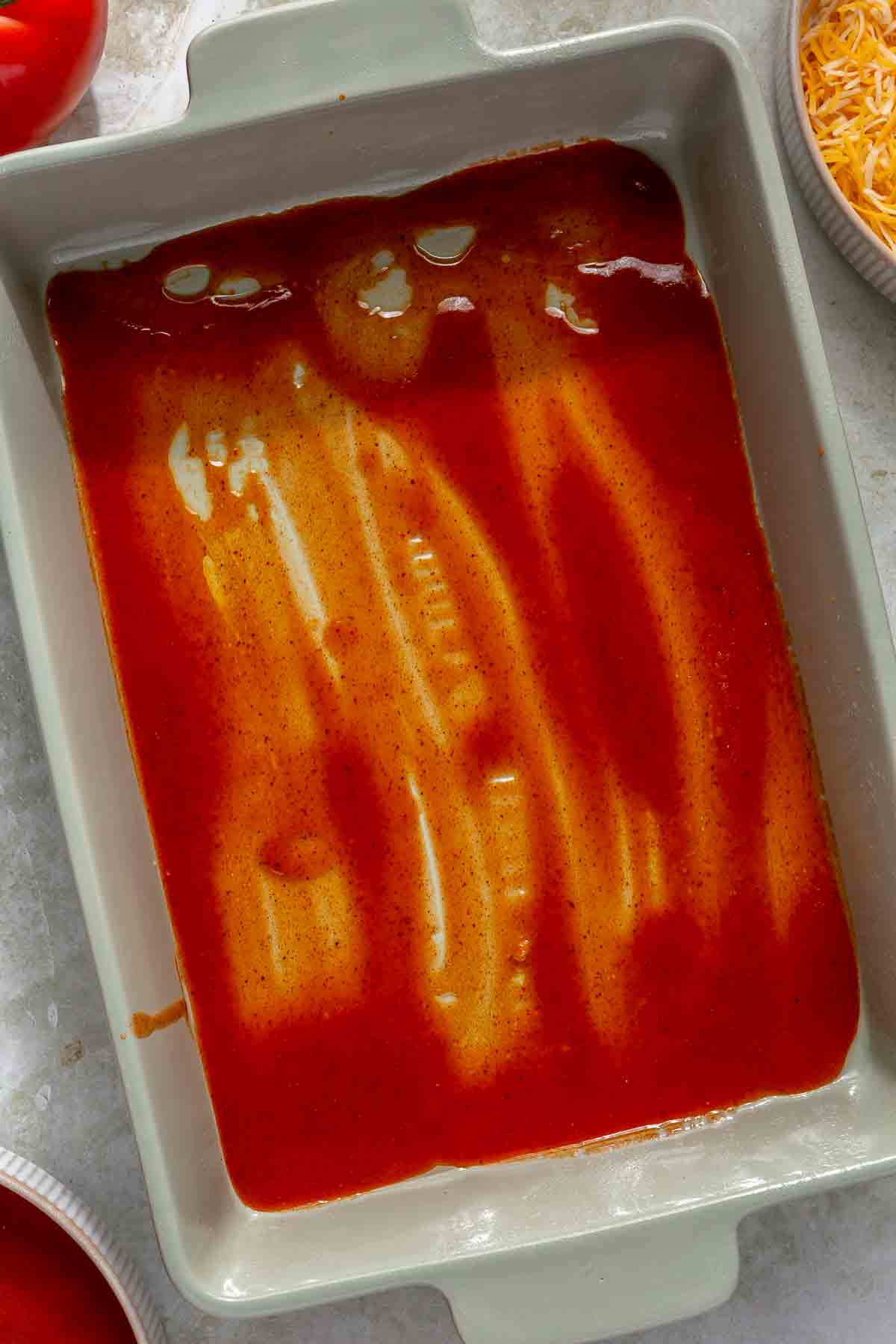 Spreading enchilada sauce in the bottom of a pan.