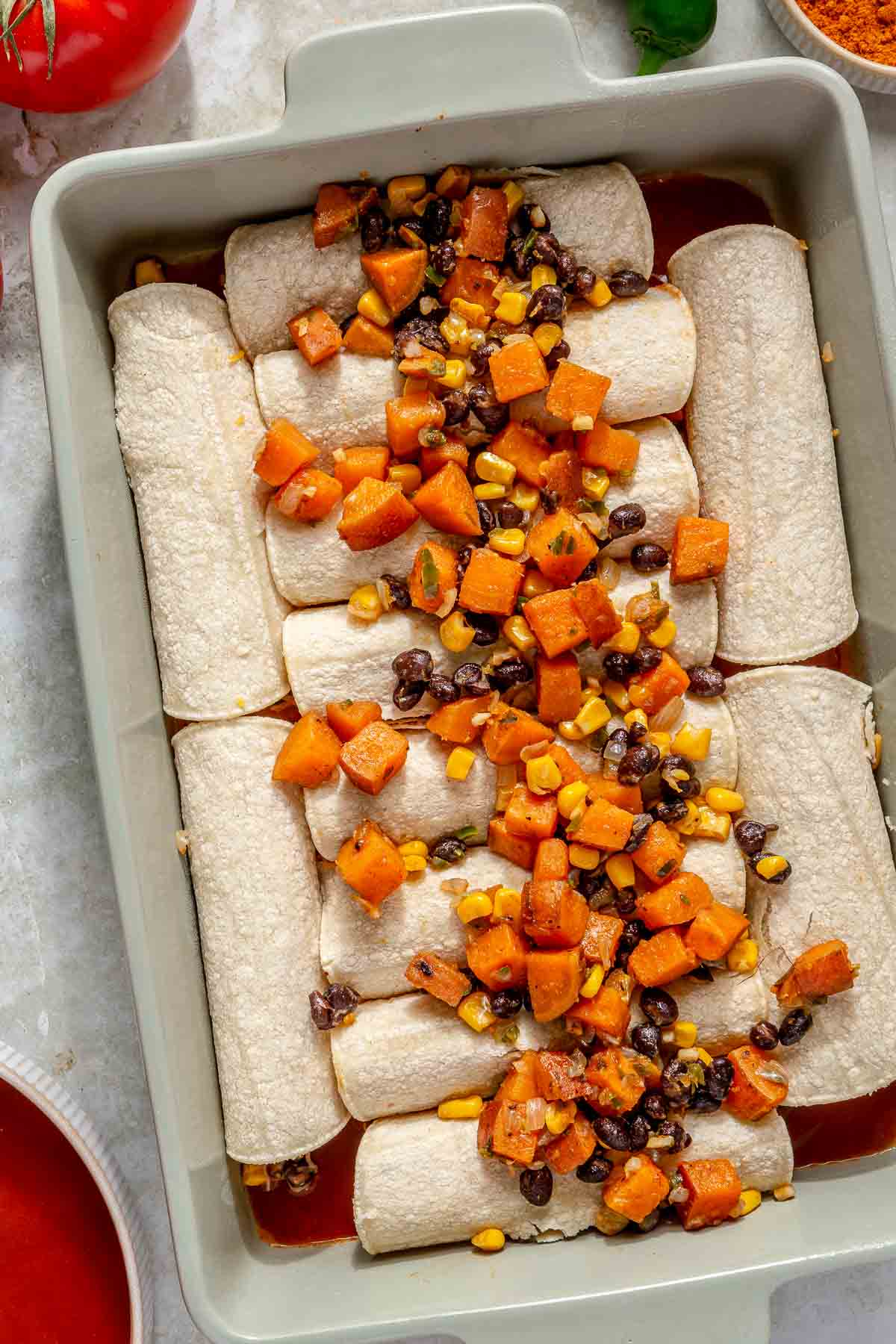 Sweet potato mixture added down the center of rolled tortillas in a pan.
