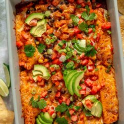 Sweet potato black bean enchiladas topped with avocado slices, green onions and diced tomatoes.