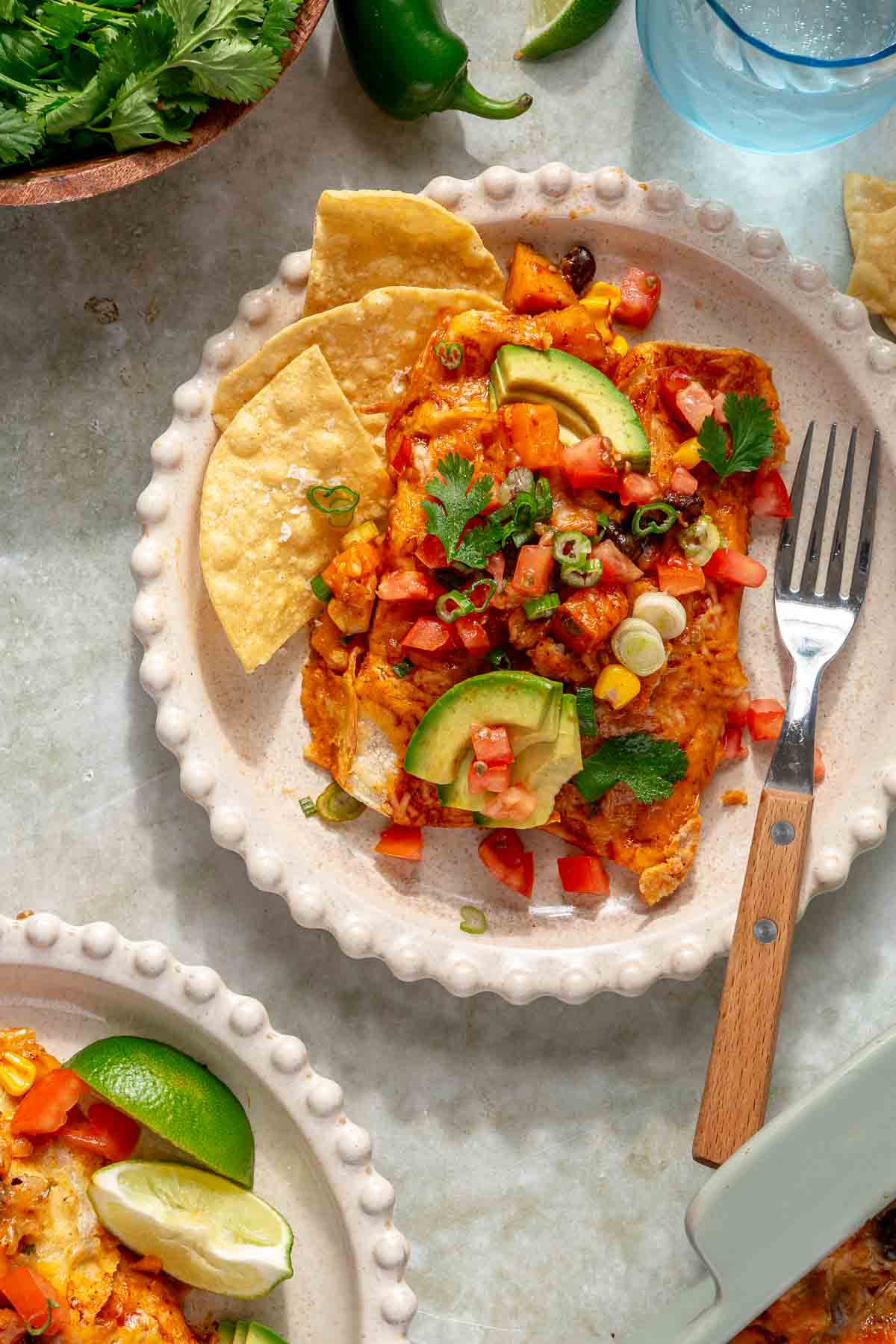 Two sweet potato black bean enchiladas served on a plate with chips.