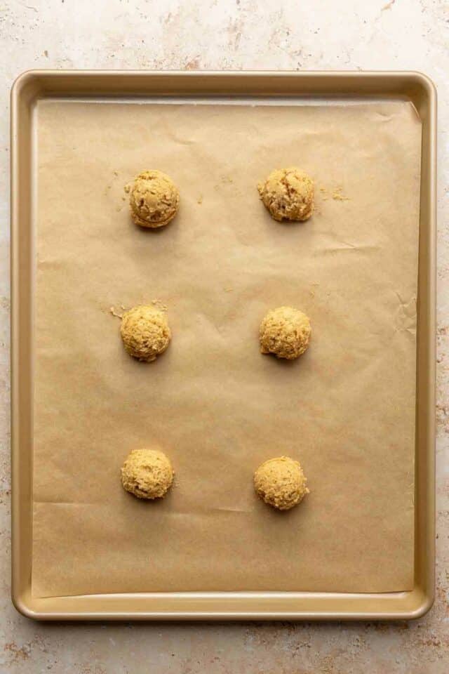 Cookie dough balls on a cookie sheet lined with parchment paper.