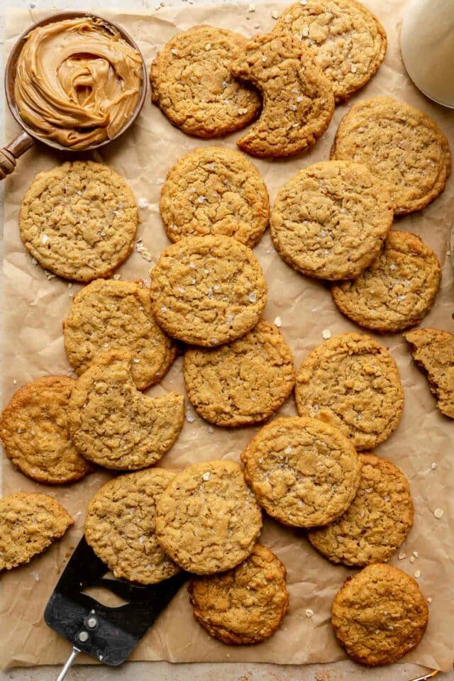 Flat cookies on parchment paper near peanut butter.