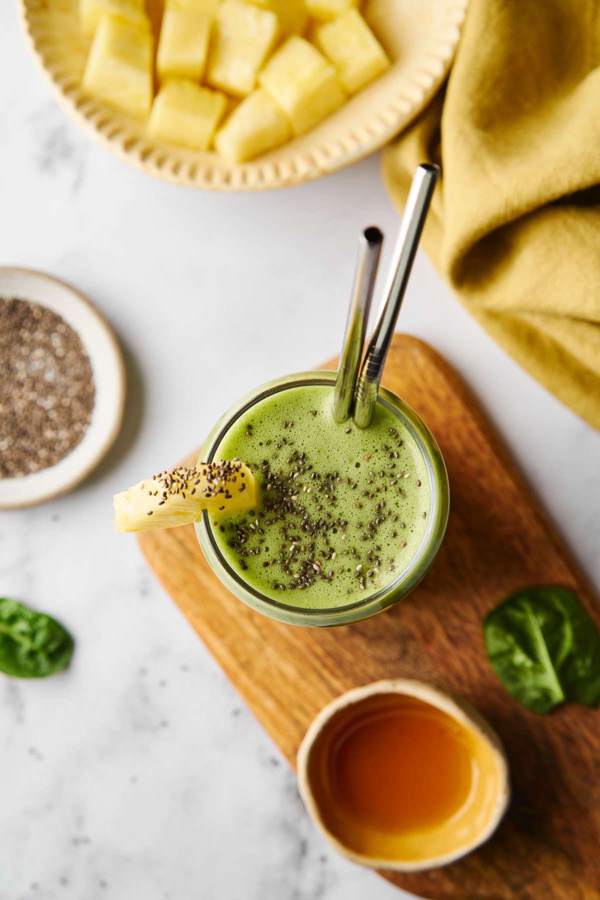An overhead view of a green smoothie garnished with chia seeds and pineapple.