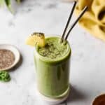 Green smoothie garnished with pineapple and chia seeds.
