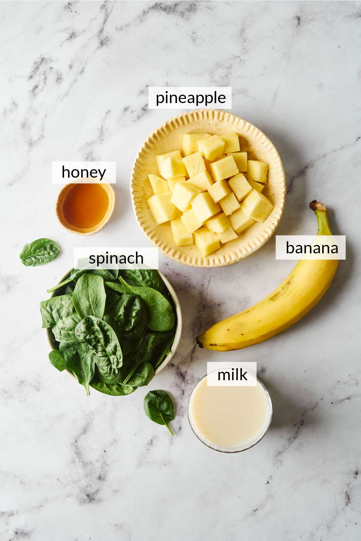 Bowls with pineapple, spinach, honey, milk and a banana.
