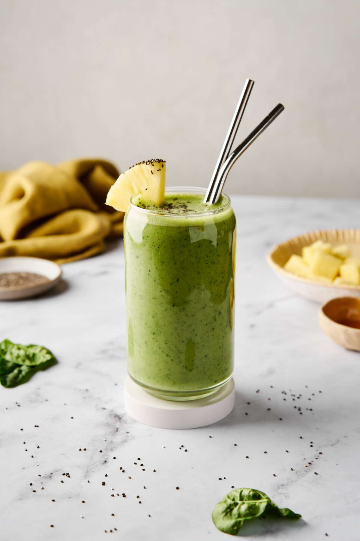 Green smoothie in a glass with two straws and a garnish of a pineapple slice.