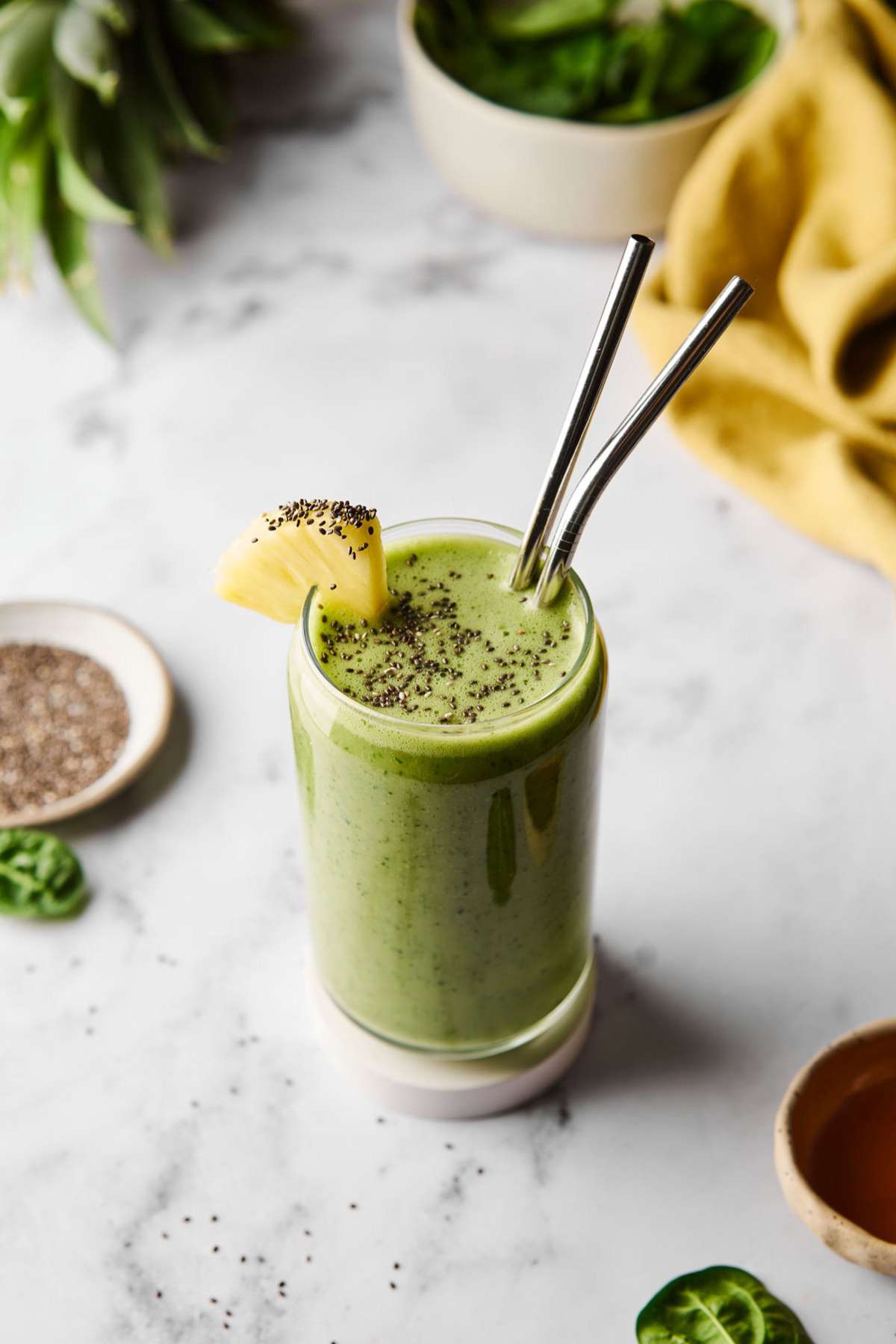 Green smoothie garnished with pineapple and chia seeds.