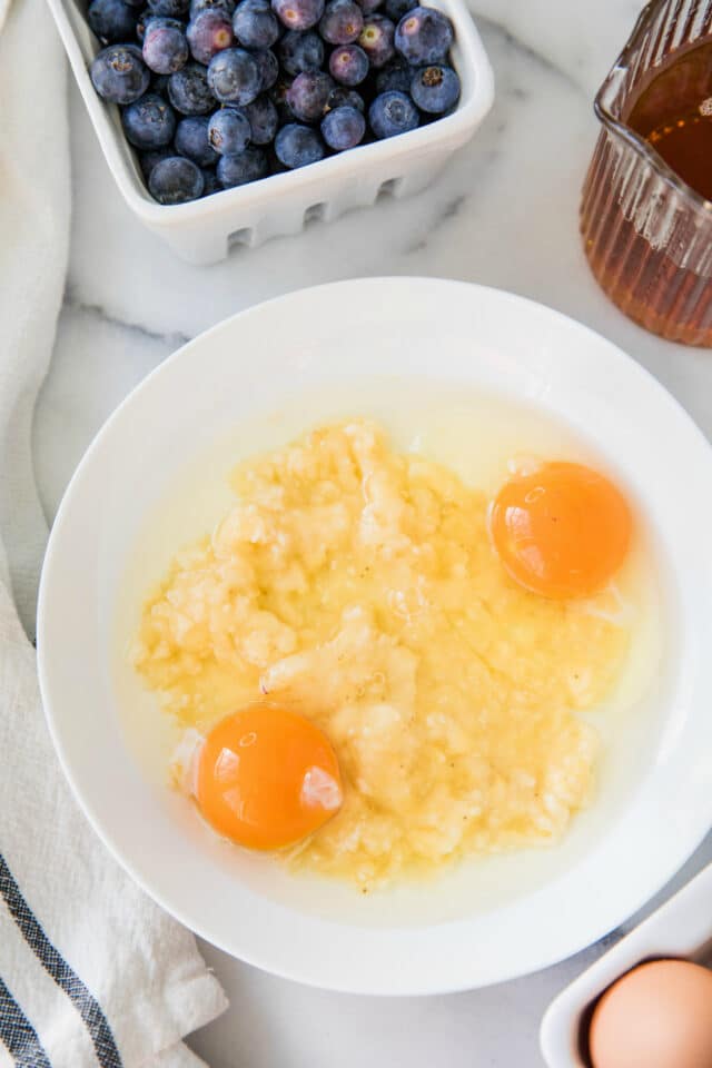 mashed banana with two eggs in a white bowl on a marble table