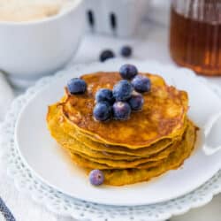 stack of thin pancakes on a white plate topped with blueberries and syrup