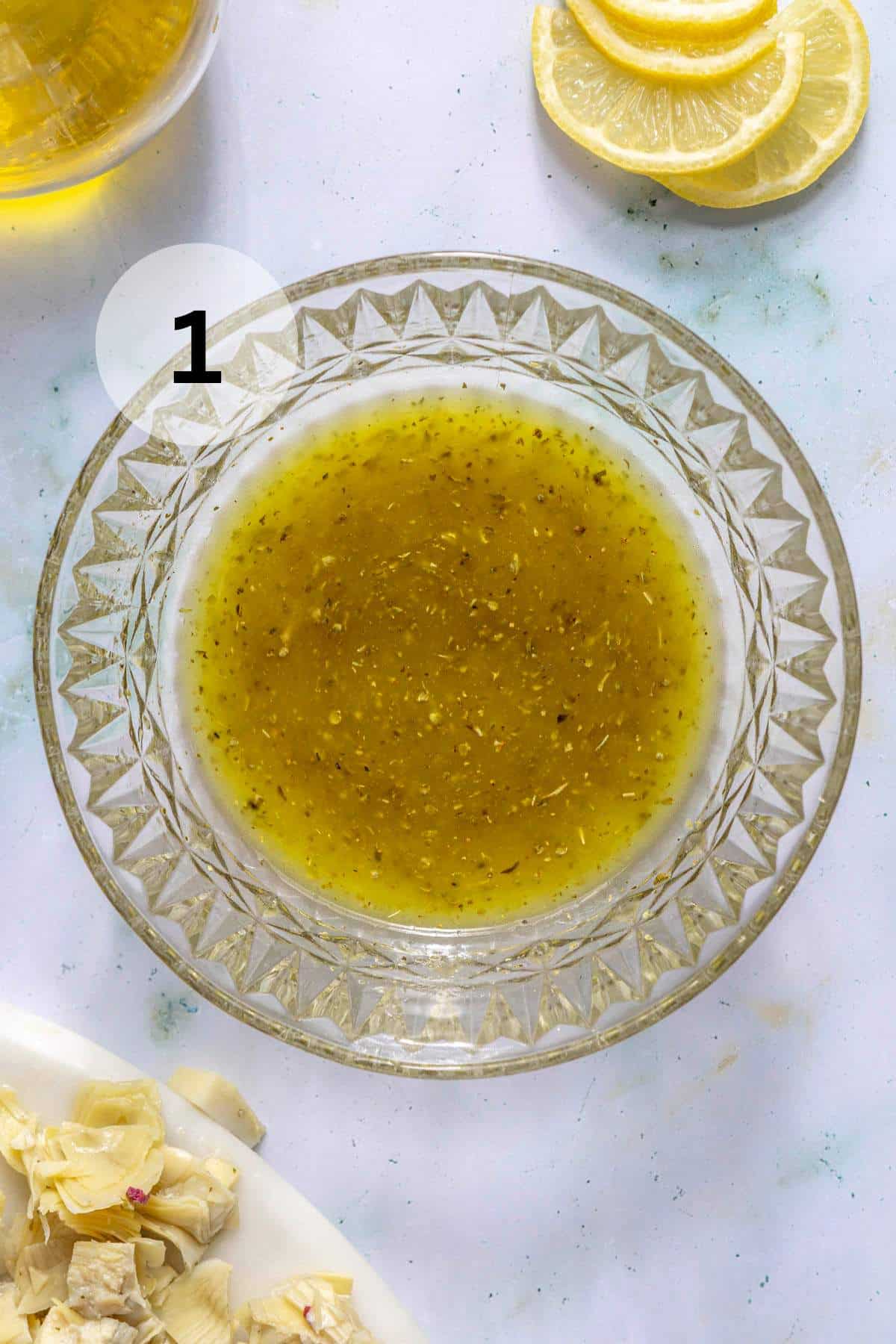 Greek dressing in a small glass bowl near slices of lemon.