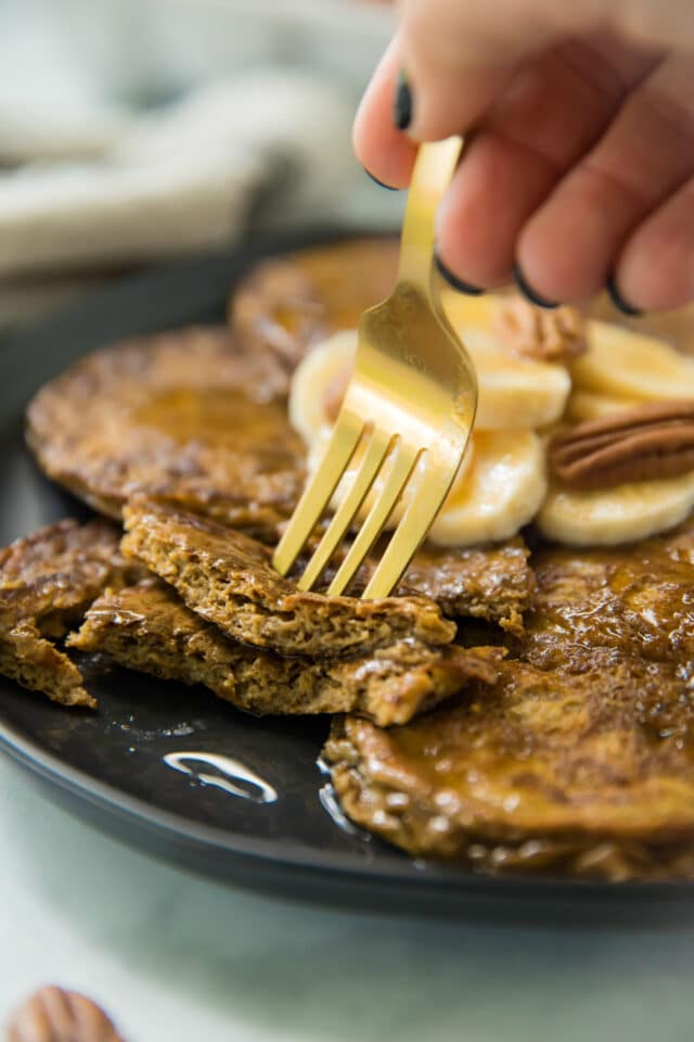 side view of Flourless Pumpkin Pancakes served on a black plate with a gold fork taking a bite out