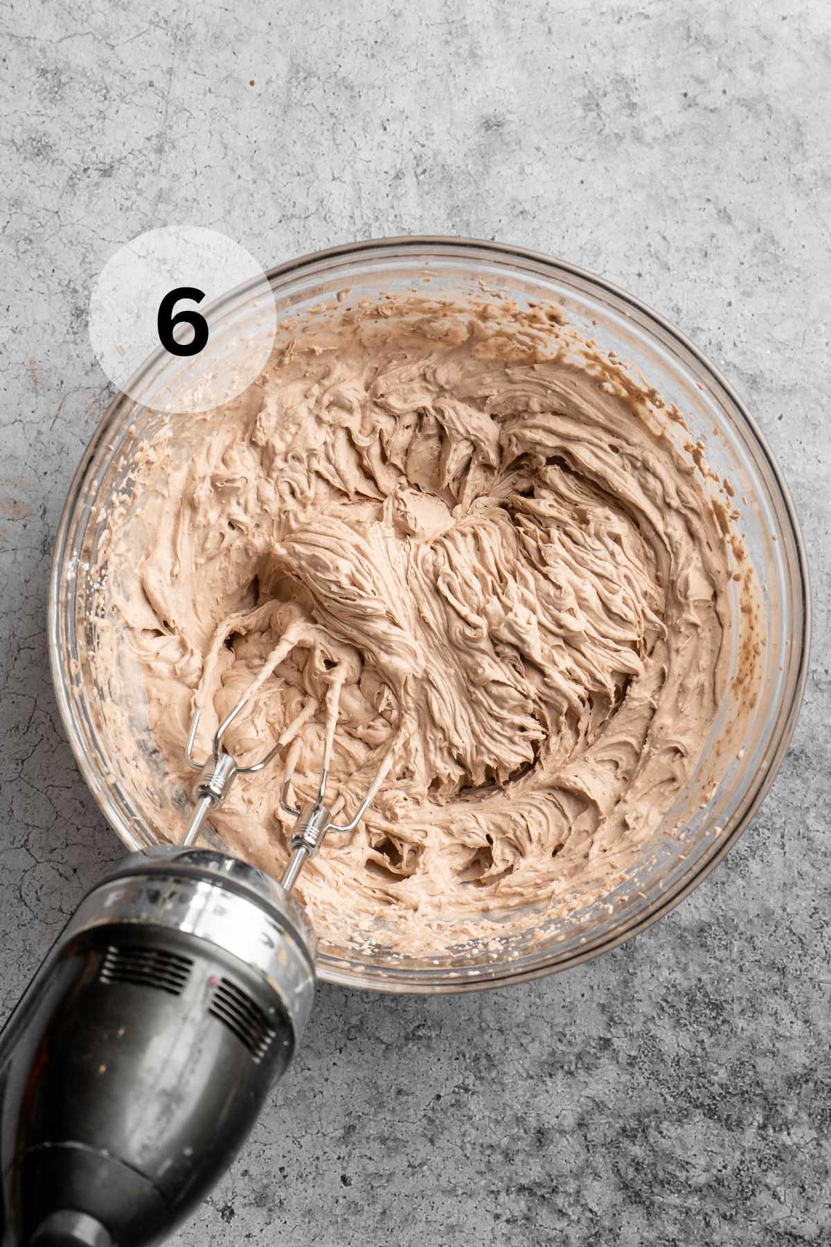Using a hand mixer to combine frosting ingredients.