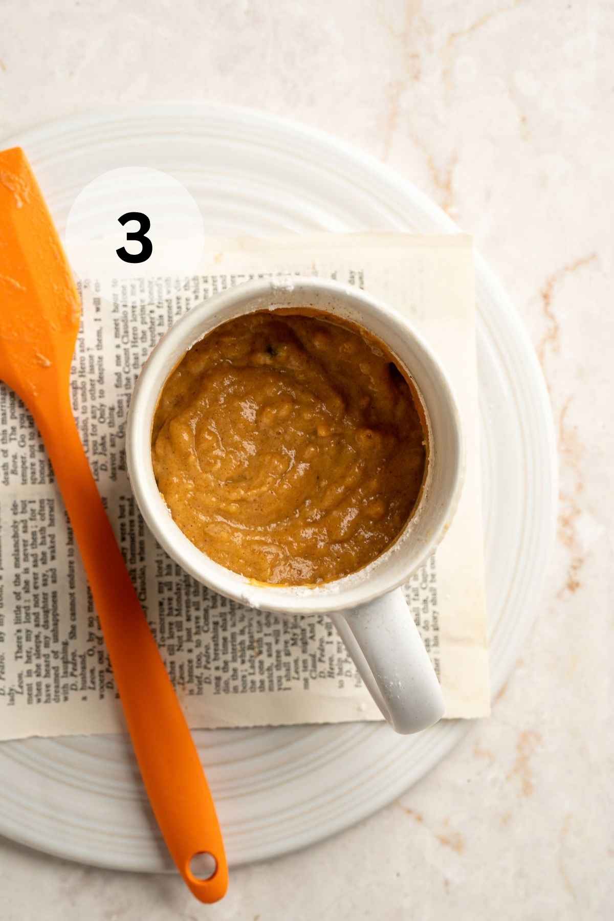 Pumpkin mug cake batter stirred in a white mug on a plate.