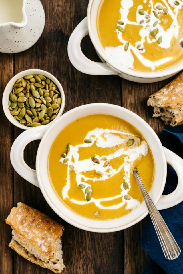 butternut squash soup served in a white bowls and topped with pumpkin seeds and cream