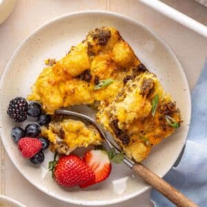 Serving of tater tot casserole on a white plate with fruit.