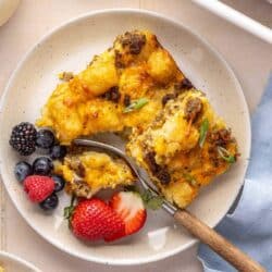 Serving of tater tot casserole on a white plate with fruit.