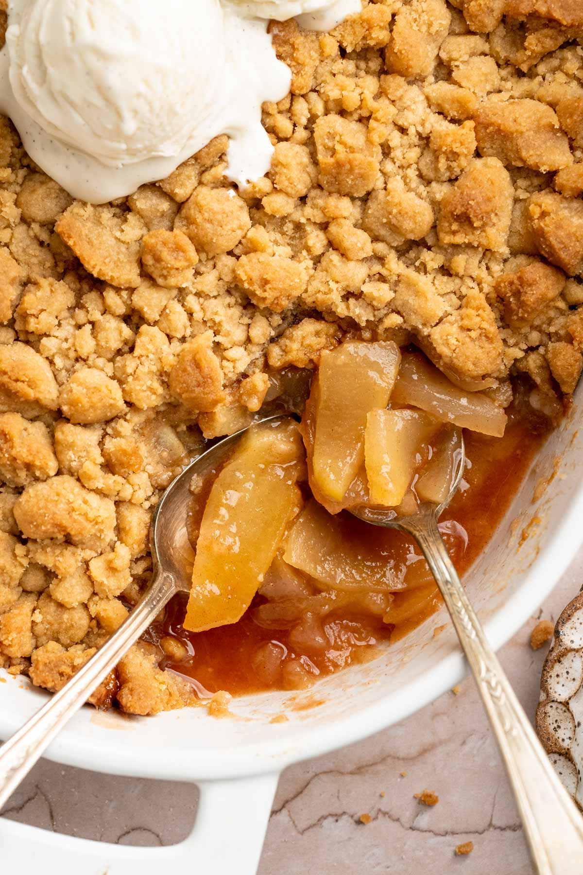 Large serving spoons in an apple crumble recipe with ice cream.
