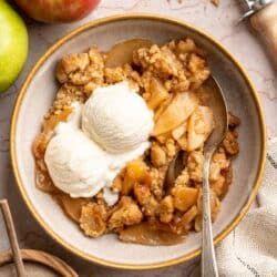 Apple crumble served in a bowl with two scoops of vanilla ice cream.