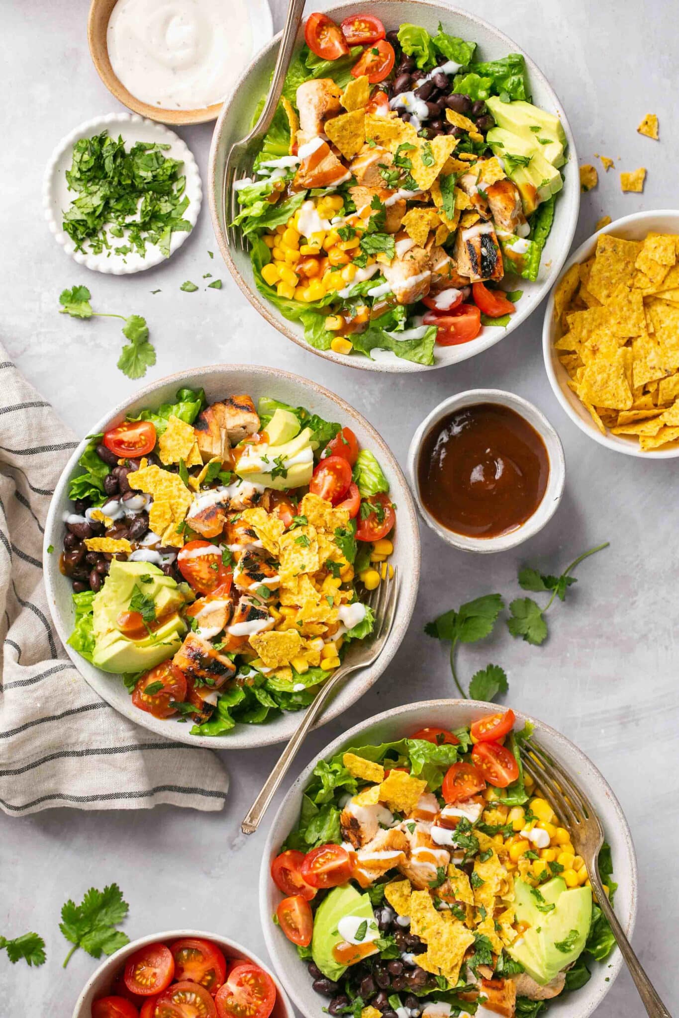 Salads in white bowls topped with grilled chicken, avocado and chips.