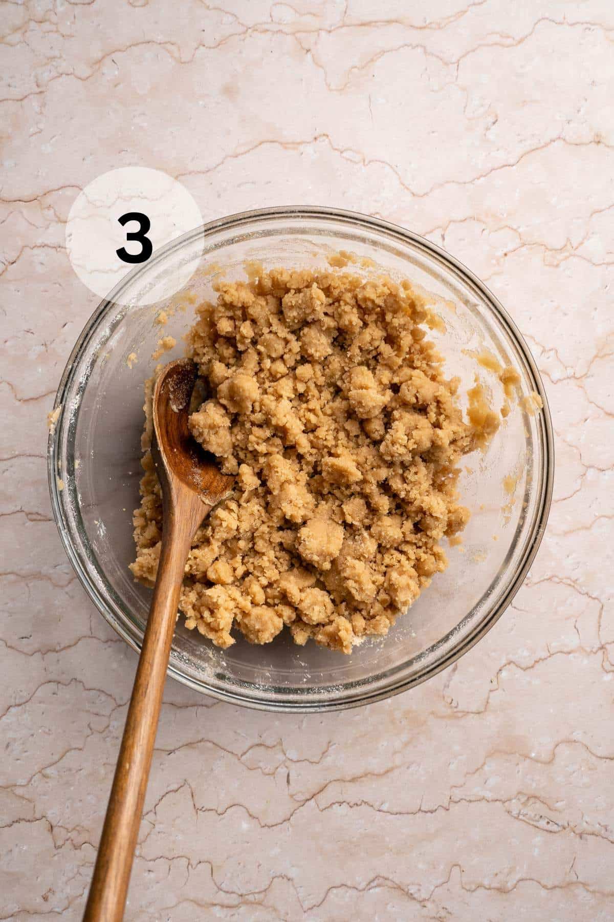 Using a wooden spoon to stir flour, brown sugar and melted butter in a small bowl.