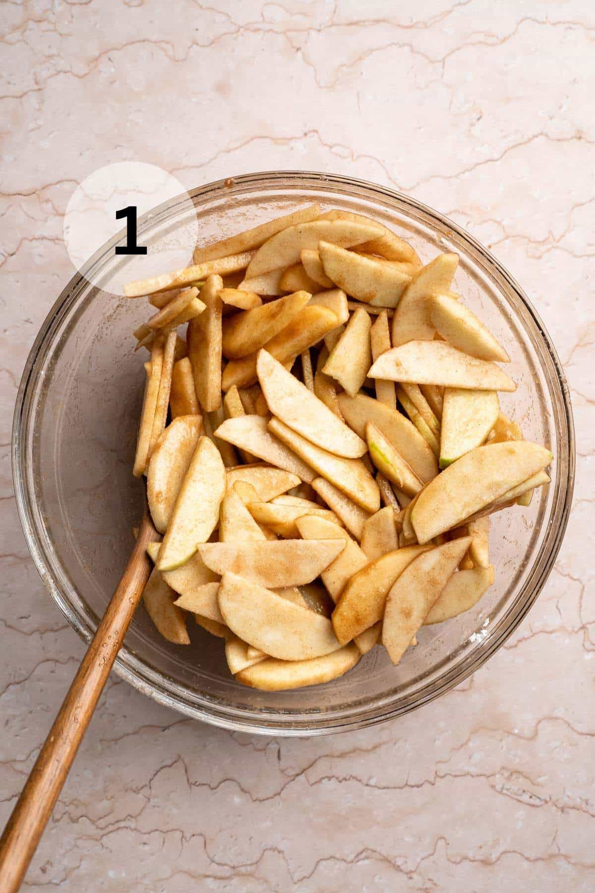 Tossing apples with spices and lemon juice in a glass bowl.