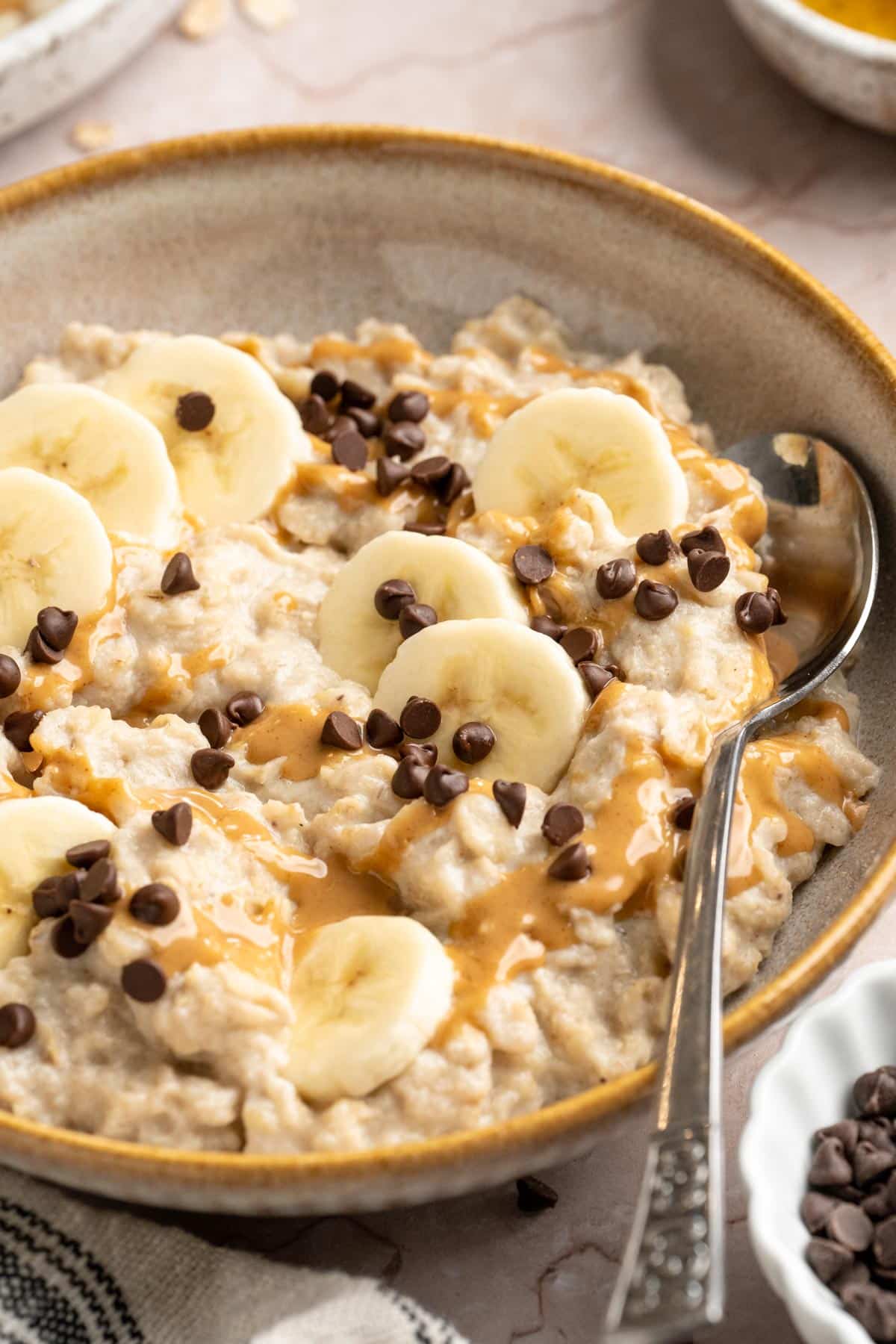 Egg white oatmeal in a bowl with a spoon topped with banana slices and mini chocolate chips.