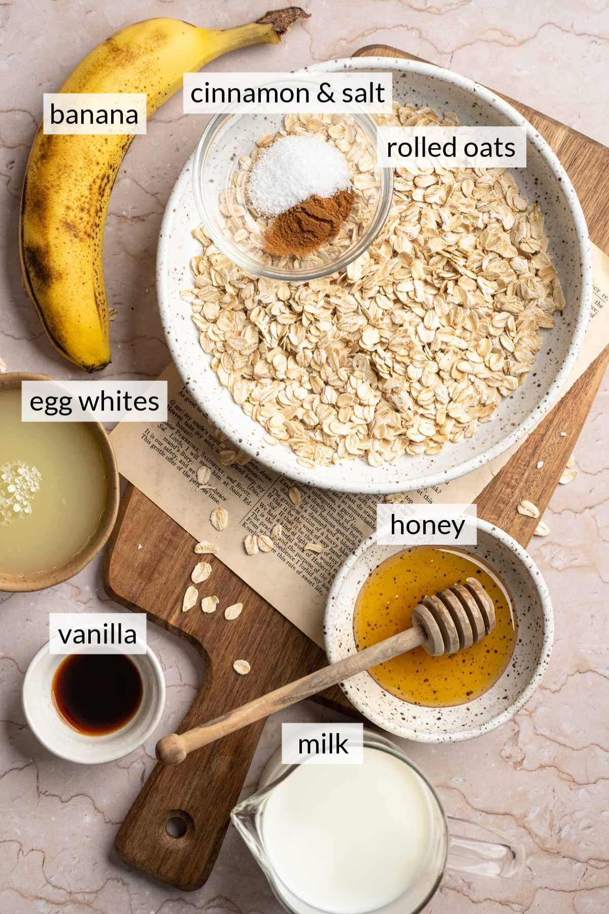 Bowls with rolled oats, honey, vanilla, milk, egg whites and spices near a banana.