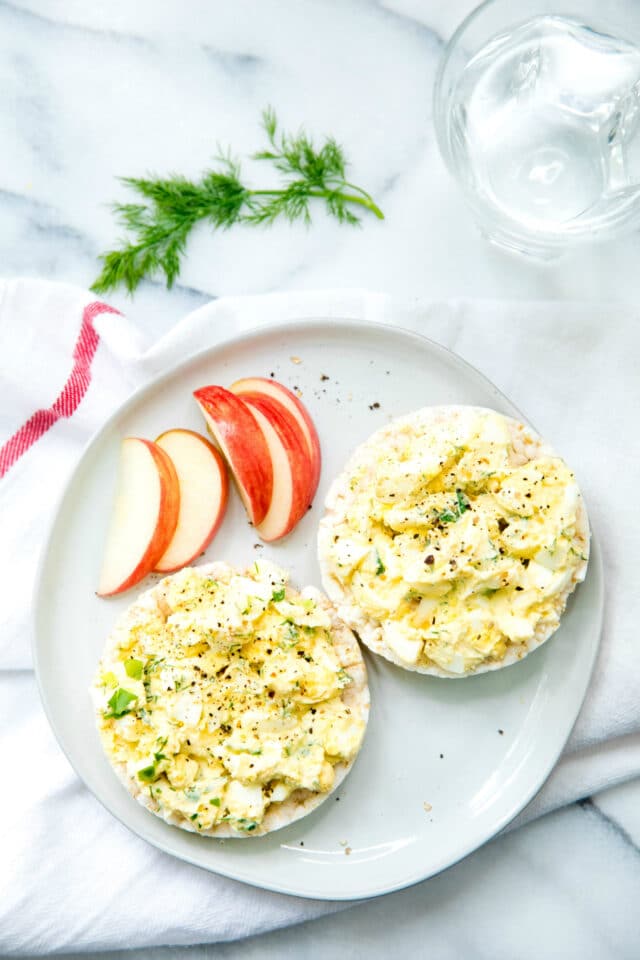 Skinny Egg Salad served on rice cakes on a white plate with sliced apple