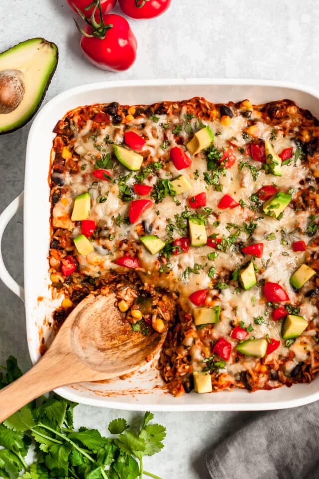 serving healthy chicken enchilada casserole with a wooden spoon