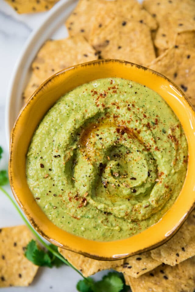 Cilantro Jalapeño Hummus topped with paprika and served in a yellow bowl with tortilla chips