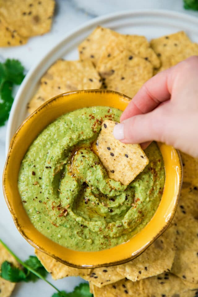 woman's hand dipping a tortilla chip in a green hummus