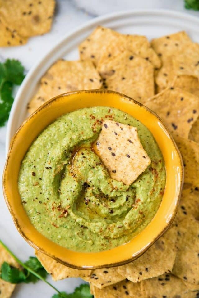 Cilantro Jalapeño Hummus in a yellow bowl with a tortilla chip dipped in the middle