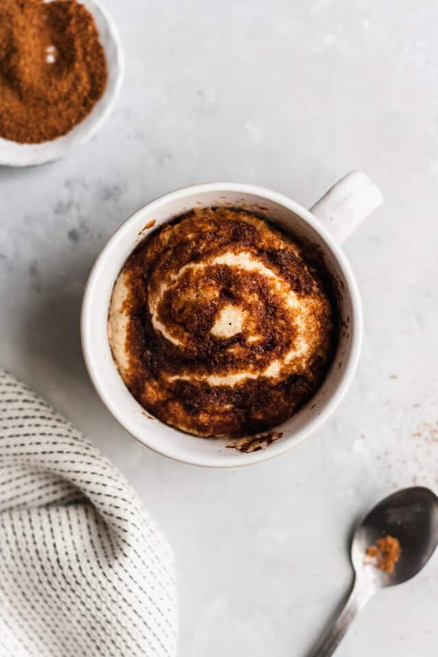 Cinnamon Roll Microwave Mug Cake in a white mug with a silver spoon on the side