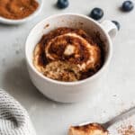 cinnamon roll microwave mug cake in a white mug with one spoonful taken out