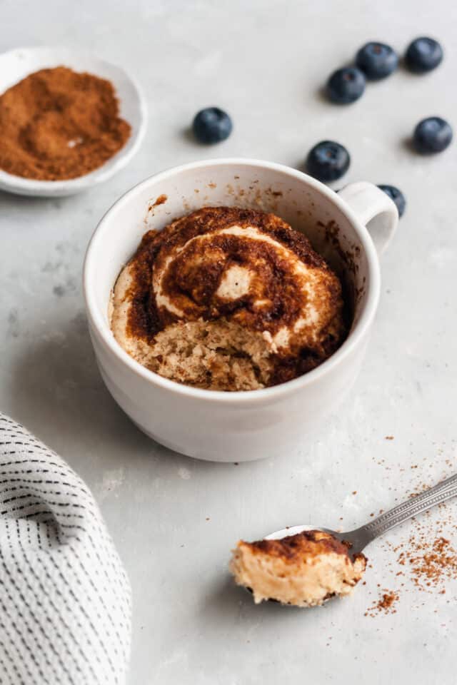 cinnamon roll microwave mug cake in a white mug with one spoonful taken out
