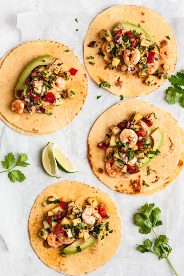 shrimp tacos made with corn tortillas and served with avocado and lime slices