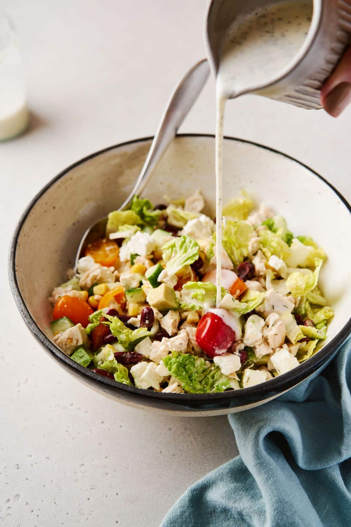 Pouring ranch dressing over a salad made with lettuce, tomatoes and chicken.