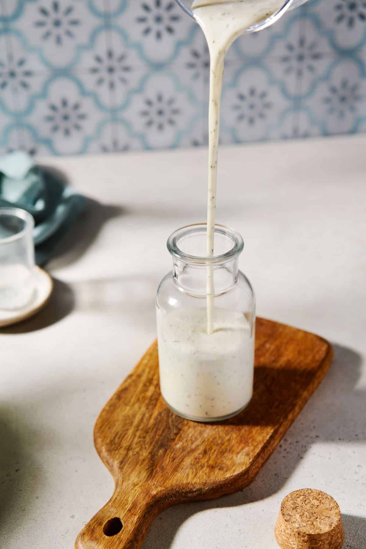 Pouring greek yogurt ranch dressing into a small jar.