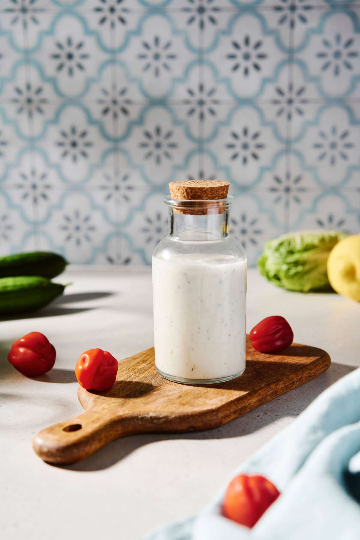 Greek yogurt in a jar on a cutting board near fresh cherry tomatoes and cucumber.
