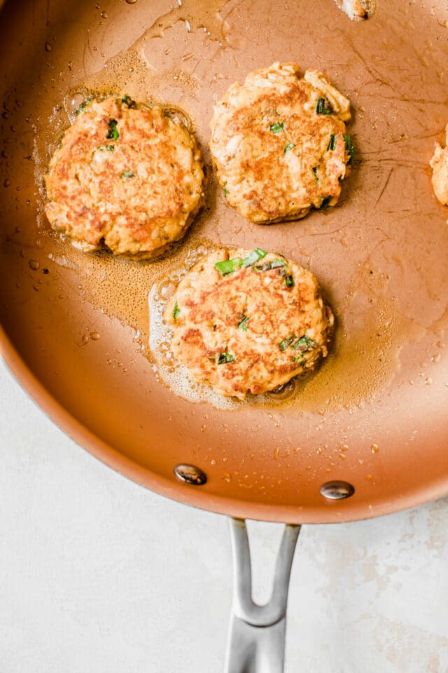 salmon patties cooking on a copper colored skillet