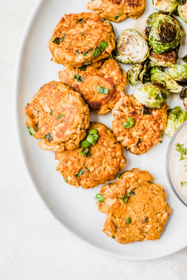 salmon cakes topped with green onion and served with roasted Brussels sprouts and dipping sauce