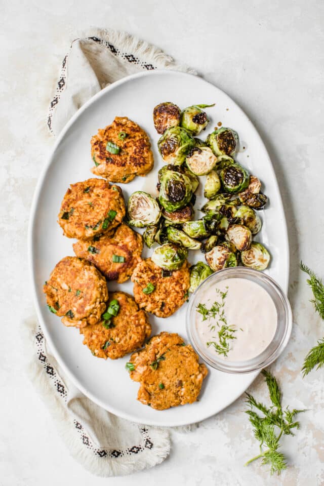 large white plate filled with sweet potato patties, roasted Brussels sprouts and dill dipping sauce