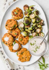 Sweet Potato Salmon Cakes served on a large white platter with Brussels sprouts and a dill dip