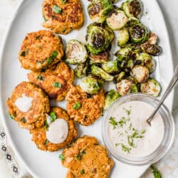Sweet Potato Salmon Cakes served on a large white platter with Brussels sprouts and a dill dip