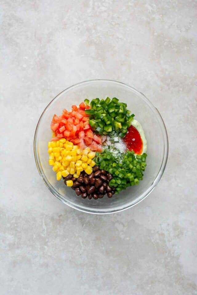 Adding black beans and fresh veggies to avocado and cottage cheese in a large bowl.