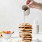 woman's hand pouring syrup over the top of a stack of pancakes