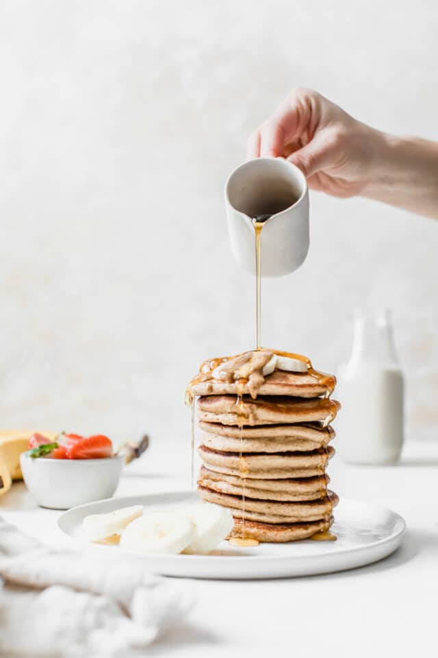 woman's hand pouring syrup over the top of a stack of pancakes