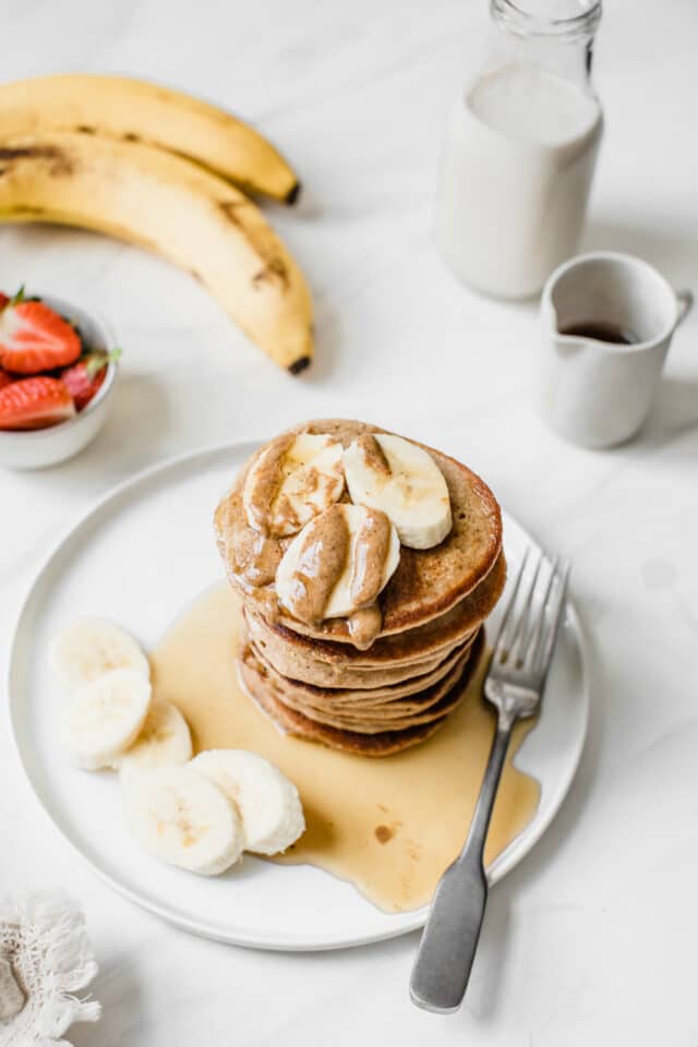 a stack of banana pancakes topped with banana slices, peanut butter and maple syrup