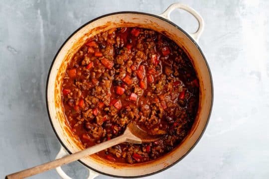 stirring Bison Chili in a large pot with a wooden spoon
