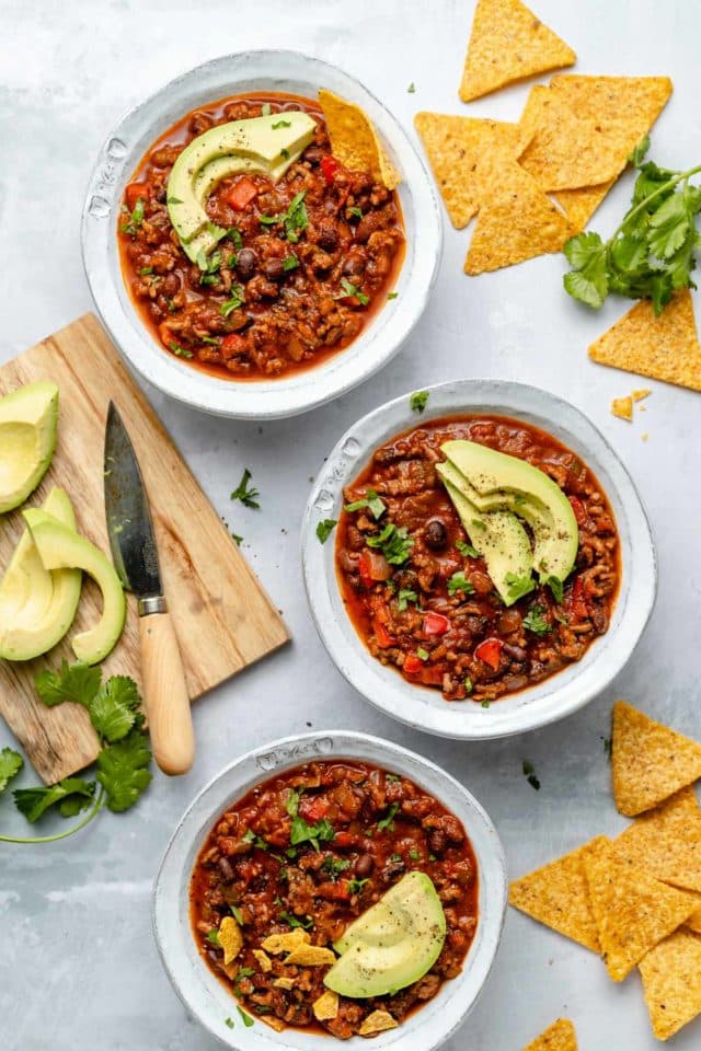 3 bowls of bison chili served with avocado slices and tortilla chips